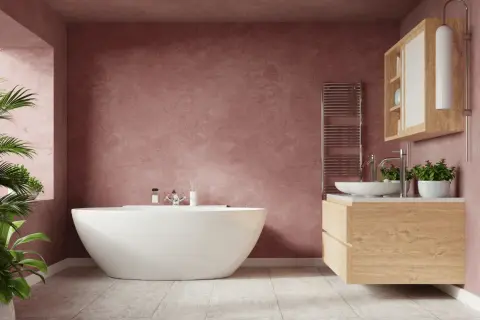 Un baño moderno con bañera independiente y tocador de madera. Las paredes de color rosa empolvado y las plantas aportan un toque acogedor a estos baños rústicos.