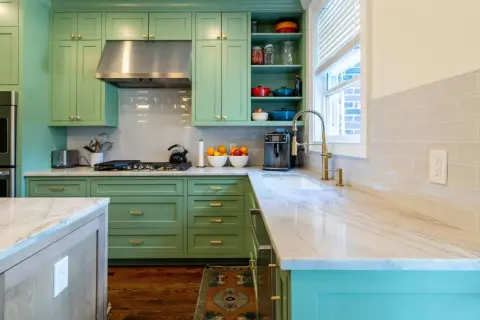 Elegante cocina verde agua y madera con encimeras de mármol, electrodomésticos de acero inoxidable y detalles dorados.