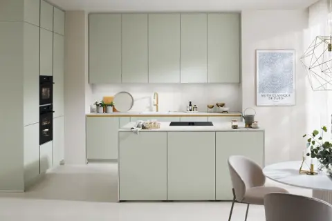 Moderna cocina verde con isla central, electrodomésticos integrados y una mesa redonda con sillas.
