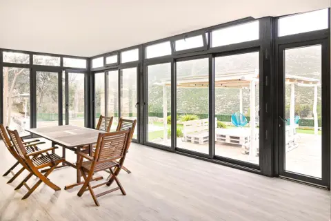 Comedor interior con mesa de madera y sillas, conectado a un jardín con porche acristalado. Precio a consultar.