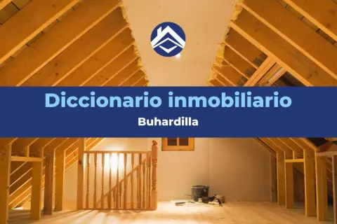 Interior de una buhardilla en construcción, con vigas de madera expuestas y una escalera. El texto indica "Diccionario inmobiliario: Buhardilla".