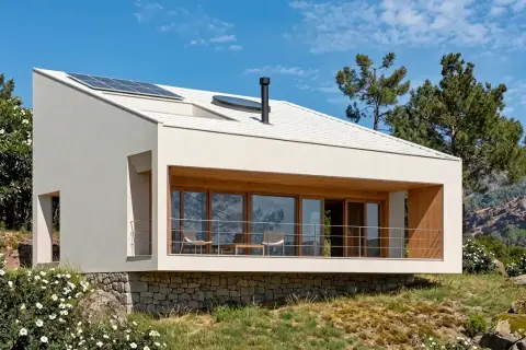 Casas de montaña modernas con paneles solares en el tejado, rodeadas de vegetación y rocas, con vistas a un paisaje montañoso.