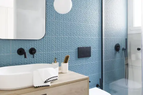Moderno baño con azulejos azules texturizados y lavabo ovalado. Ideas para cuartos de baño pequeños: grifería negra, espejo redondeado y ducha de cristal.