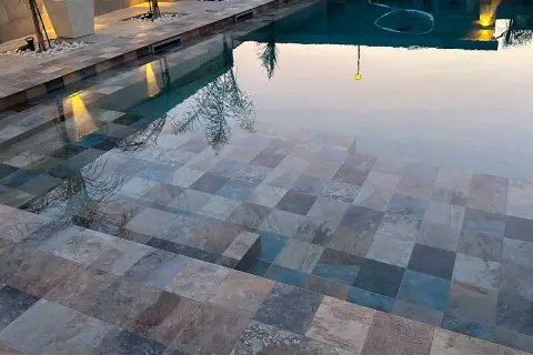 Escalones de baldosas de piedra entran en unas piscinas interiores, reflejando luces y árboles.