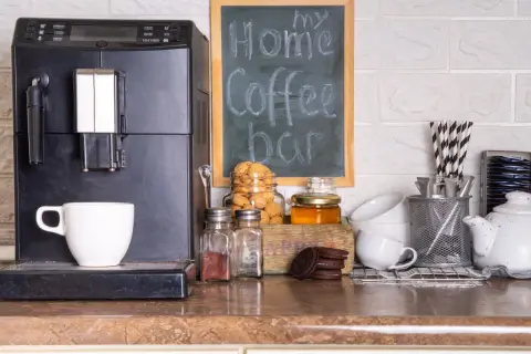 Máquina de café, taza, galletas y un letrero de "my Home Coffee bar" en un rincón de la cocina.