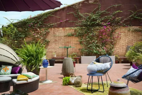 Acogedor **diseño terraza exterior** con muebles de ratán, sillas azules, plantas exuberantes y detalles decorativos en ladrillo.