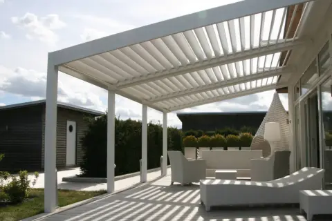 Un moderno porche patio de casa con muebles blancos de mimbre y una pérgola de listones.