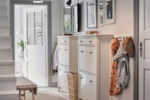 Elegante decoración de entradas y recibidores: zapateros blancos, perchero con abrigos y un banco de madera invitan a entrar.