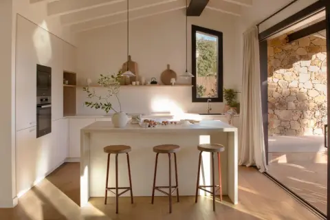 Cocina luminosa con isla central, taburetes y vistas a un patio de piedra, ideal para casas de campo modernas.
