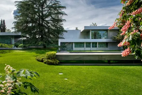 Casa moderna rodeada de jardines bonitos, césped verde y flores rosadas.