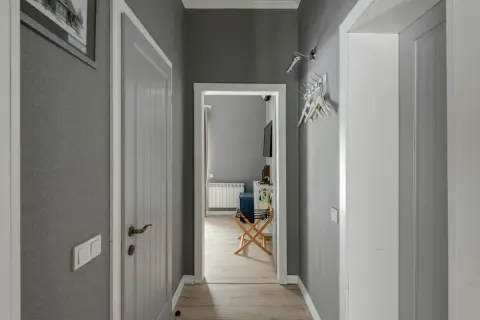 Pasillos con encanto, con paredes grises, puertas blancas y un cuadro en la pared. Se vislumbra una habitación con un radiador y un banco.