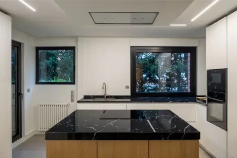 Cocina moderna con **fregadero en isla** de mármol negro y encimeras a juego. Muebles blancos y electrodomésticos integrados.