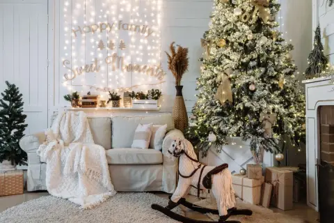Ideas para decorar mi casa en navidad: árbol nevado, luces cálidas, sofá acogedor, caballito de madera y regalos.