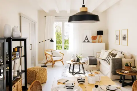 Salón luminoso con decoración de casas estilo nórdico moderno. Sofá beige, sillón de mimbre, mesa de centro redonda y estantería negra.