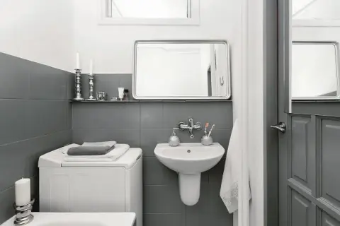 Baño moderno con azulejos grises, lavadora y lavabo. Un ejemplo de reformas de baños antes y después, con un estilo minimalista y funcional.