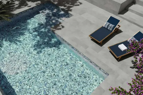 Modernas ideas de piscinas: piscina con mosaico azul brillante, tumbonas y flores moradas.