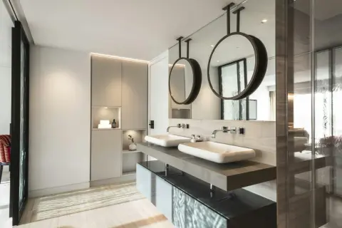 Un moderno baño con dos lavabos sobre encimera de piedra, espejos circulares colgantes y armarios integrados. Se puede hacer un baño en una habitación así.