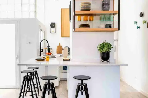 Cocinas sin muebles altos, con una isla central, taburetes negros y estanterías abiertas con vajilla.