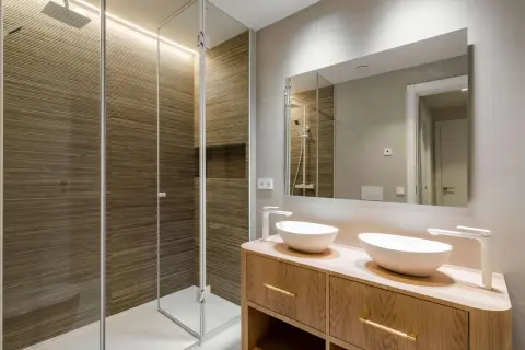 Baños pequeños con encanto: ducha con paredes de madera acanalada y tocador de madera con dos lavabos blancos.