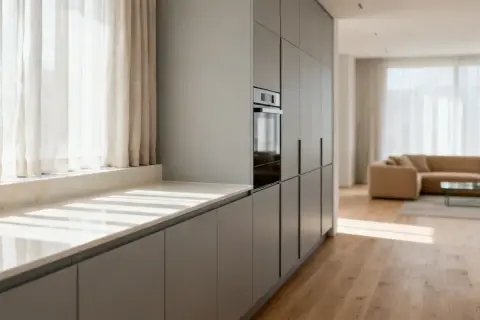 Cocina moderna con armarios grises y una encimera de mármol clara. La luz del sol entra por las cortinas, creando un ambiente acogedor.