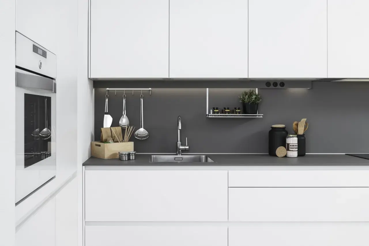 Moderna cocina blanca y gris con electrodomésticos integrados, fregadero de acero inoxidable y utensilios de cocina colgados.