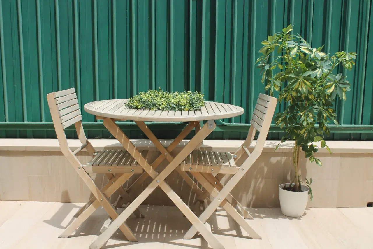 Mesa y sillas de madera en un rincón acogedor, ideal para disfrutar de terrazas con encanto. Una planta verde aporta vida.