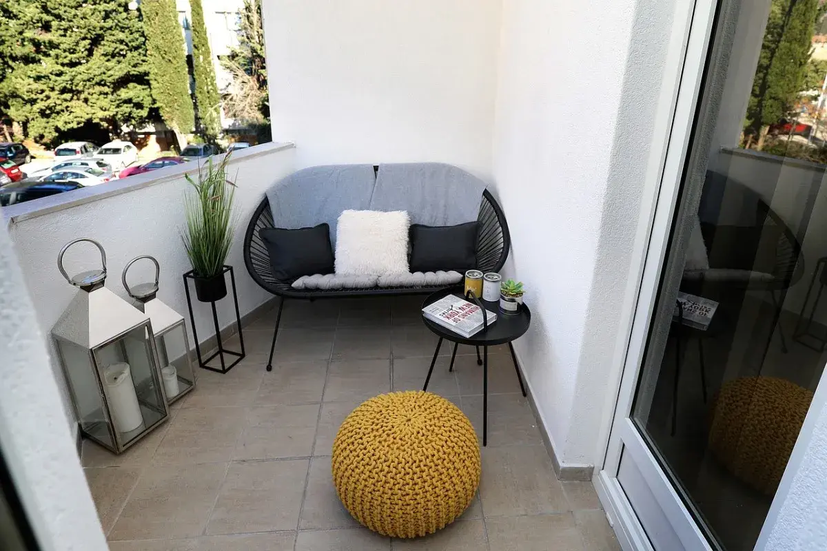 Acogedor rincón en unas terrazas pequeñas con encanto: sofá negro, cojines, mesa auxiliar con libro y plantas, y un puf amarillo.