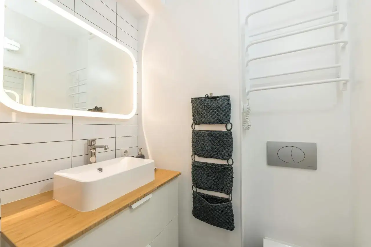 Moderno baño pequeño con lavabo sobre mueble de madera, espejo iluminado y organizador de pared.