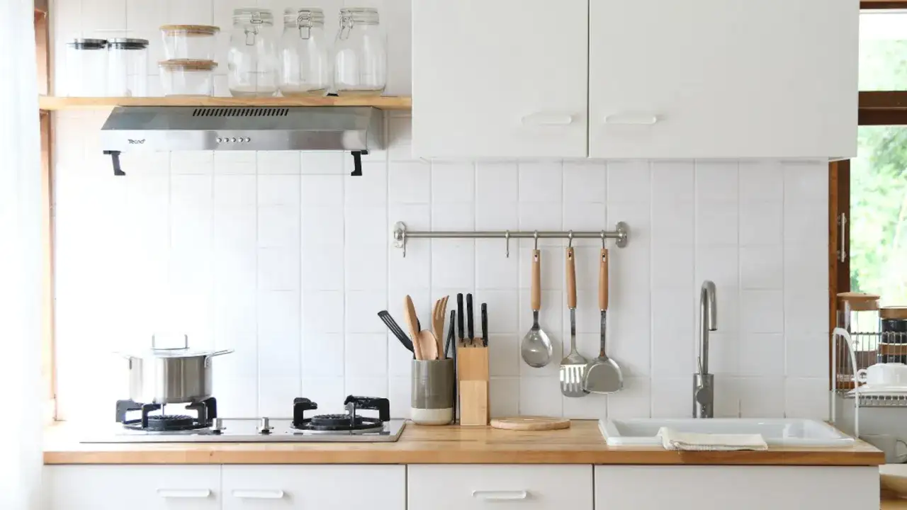 Cocinas pequeñas y funcionales: encimera de madera, fregadero, cocina de gas, utensilios y armarios blancos.