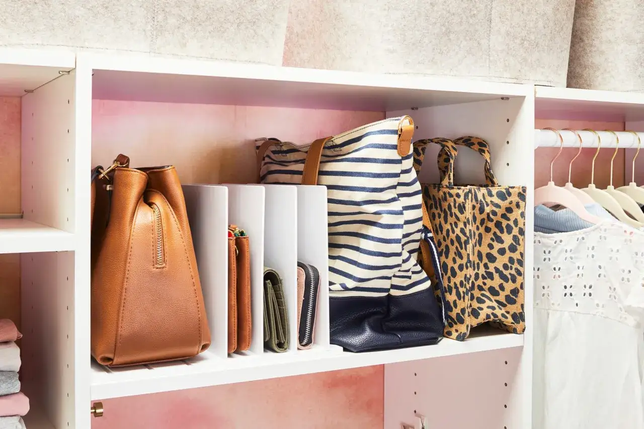 Estantería blanca con separadores para organizar bolsos. Se ven un bolso marrón, carteras y bolsos de rayas y leopardo.