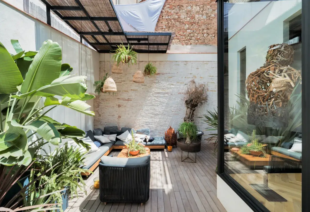 Un rincón acogedor con sofás, plantas exuberantes y lámparas de mimbre. Un espacio ideal para disfrutar de terrazas con encanto.