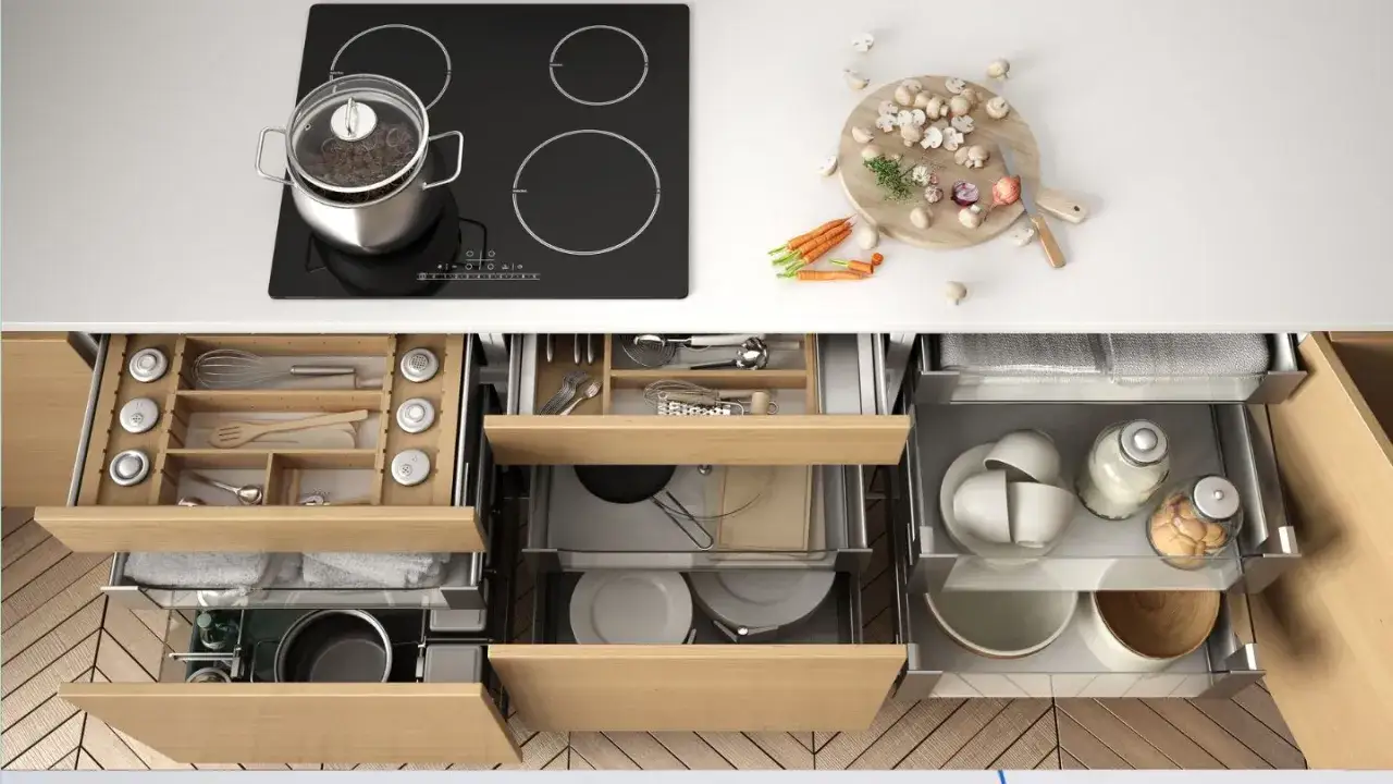 Organización inteligente para cocinas pequeñas: cajones con compartimentos para utensilios, ollas y vajilla, junto a una placa de inducción y ingredientes frescos.