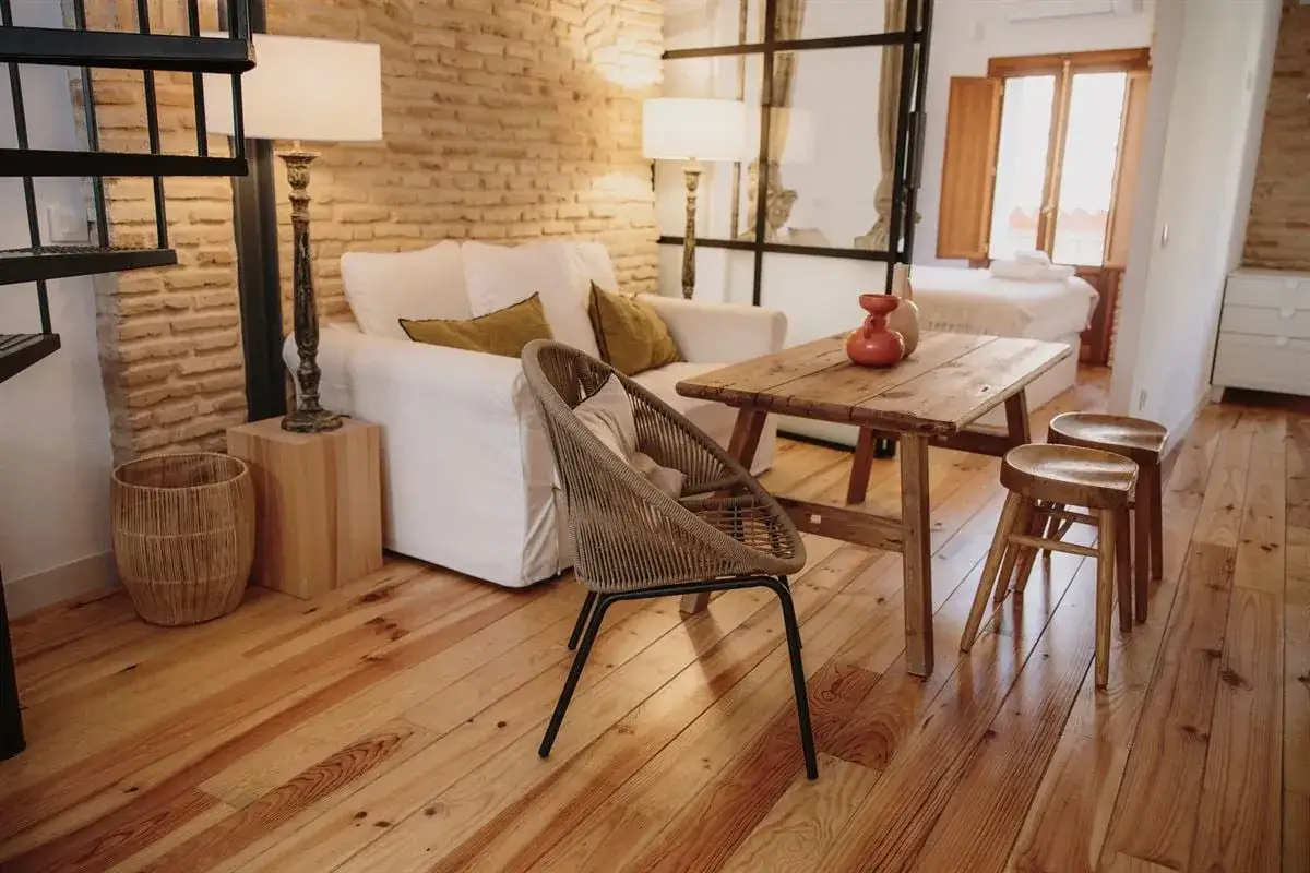 Acogedor salón con sofá blanco, mesa rústica y silla de mimbre. Un ejemplo de diseño de interiores que combina texturas naturales y luz cálida.