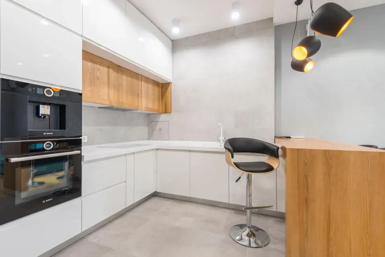Moderna cocina blanca y madera con electrodomésticos integrados, barra de desayuno y taburete.