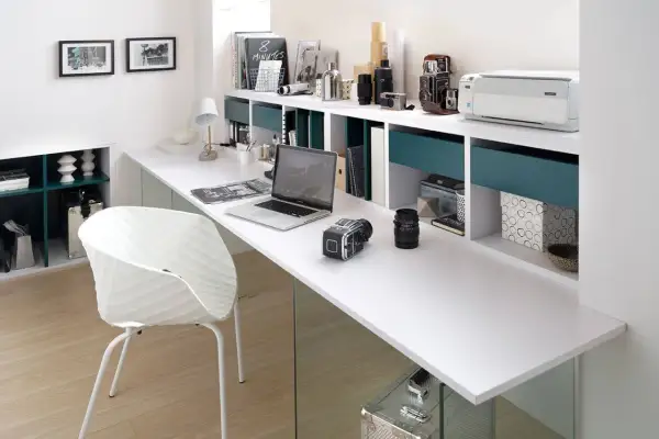 Un moderno despacho en buhardilla con un portátil, cámaras, impresora y una silla blanca.