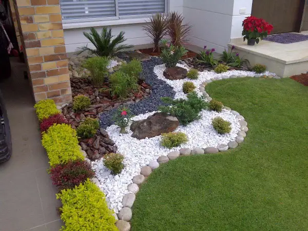 Un jardín moderno con grava blanca, rocas, plantas verdes y flores rojas, diseñado por paisajistas de jardines.