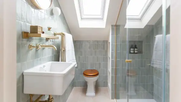 Elegantes mini aseos de cortesía con azulejos verde menta, lavabo blanco, ducha acristalada y luz cenital.