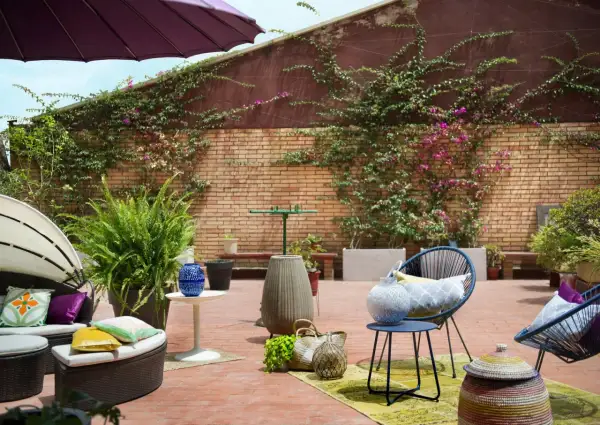 Acogedor **diseño terraza exterior** con muebles de ratán, sillas azules, plantas exuberantes y detalles decorativos en ladrillo.