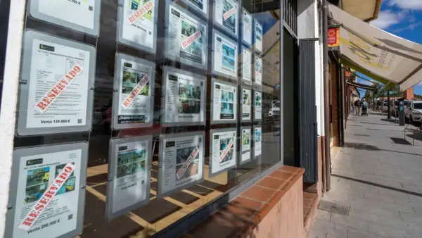 Escaparate de inmobiliaria con anuncios de venta de casas, muchos marcados como "RESERVADO". Se vislumbra una casa señorial en uno de los carteles.