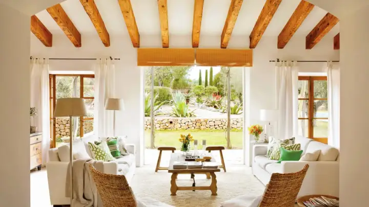Salón con vigas de madera y vistas a un jardín exuberante, reflejo de la arquitectura mediterránea.