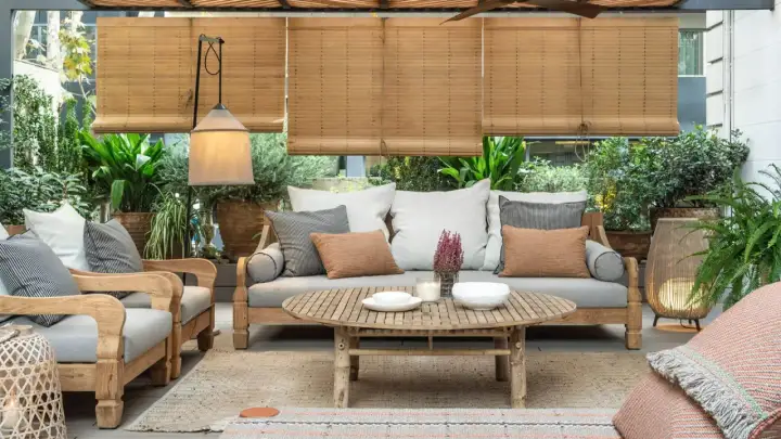 Acogedora terraza estilo mediterráneo con sofá, sillones de madera, mesa de centro y abundante vegetación.