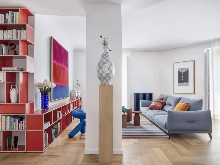 Estudios de arquitectura: sala de estar moderna con sofá azul, alfombra de rayas, estanterías rojas y arte abstracto.